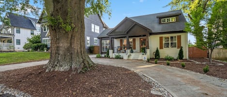 Una casa residencial con un gran árbol en el patio delantero, un césped bien cuidado y un camino de entrada.