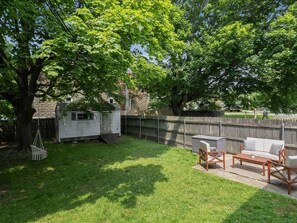 Ein Garten mit einer Holzterrasse, einem Grill und Gartenmöbeln.