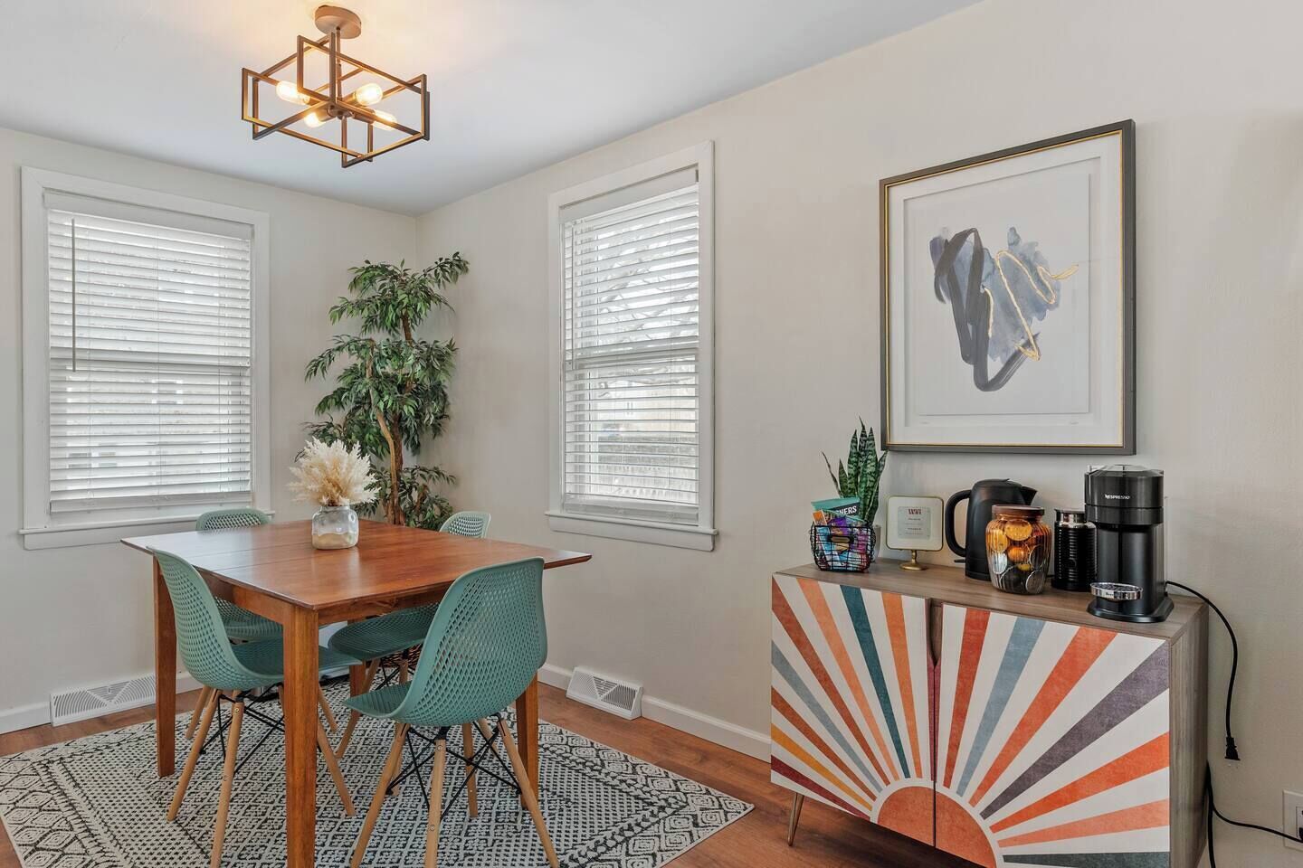 A dining area with a wooden table and chairs, a potted plant, and a colorful cabinet with a coffee maker.