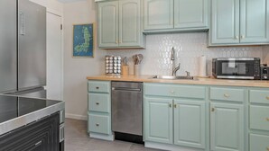 Uma cozinha com armários azul-turquesa, eletrodomésticos de aço inoxidável e backsplash de azulejo.