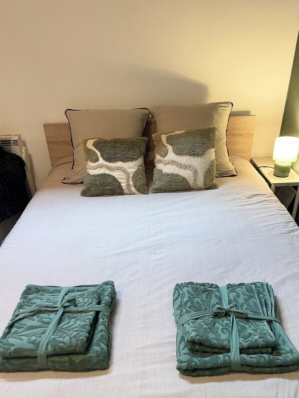 A neatly made bed with two pillows, a bedside lamp, and two folded towels on the bed.