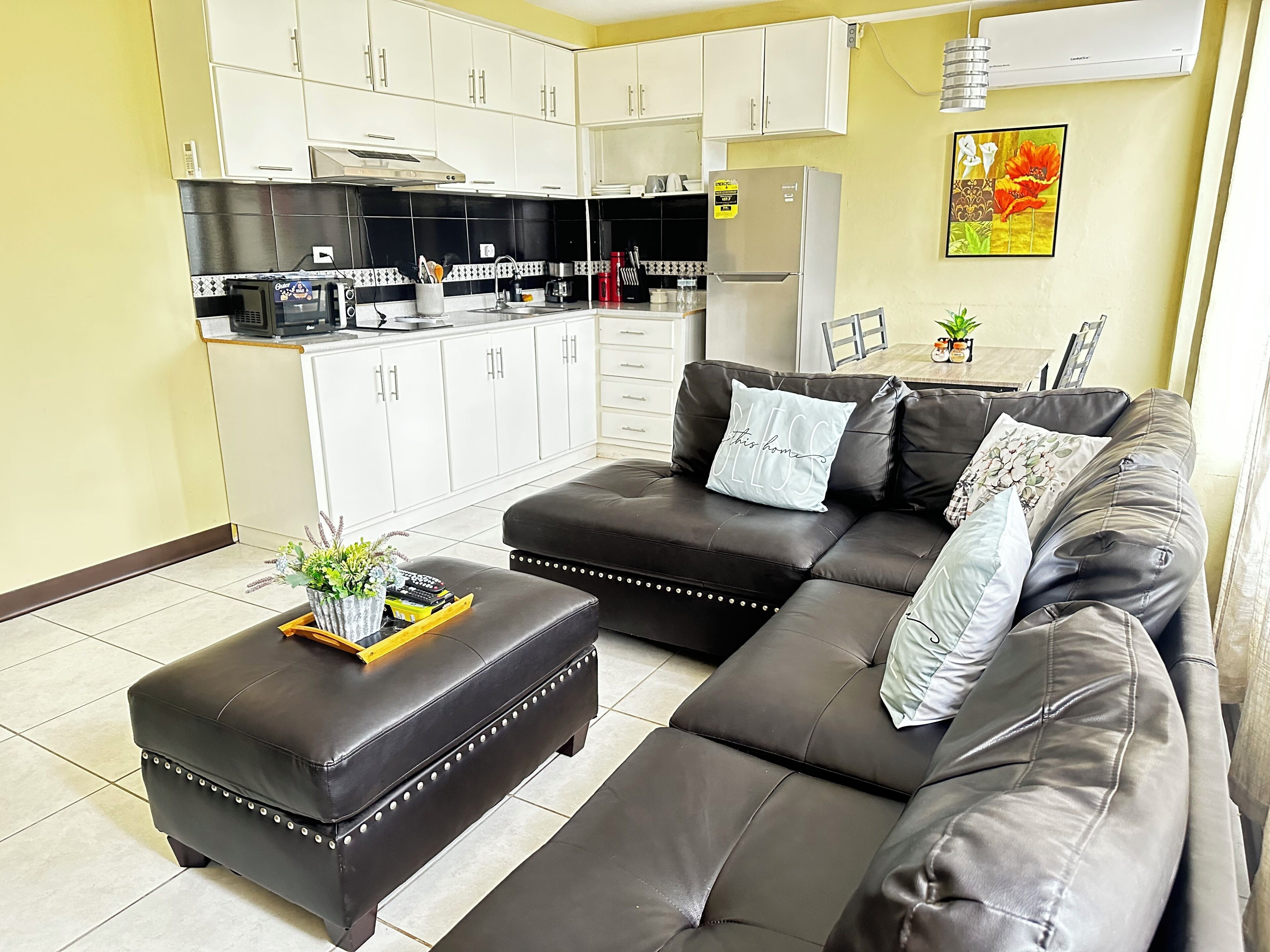 Una sala de estar moderna con un sofá seccional, una mesa de centro y una cocina con armarios blancos y electrodomésticos negros.