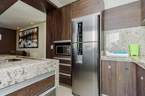 A modern kitchen with a stainless steel refrigerator, a microwave, and granite countertops. - Apto com Piscina e Garagem no Roçado (São José)
