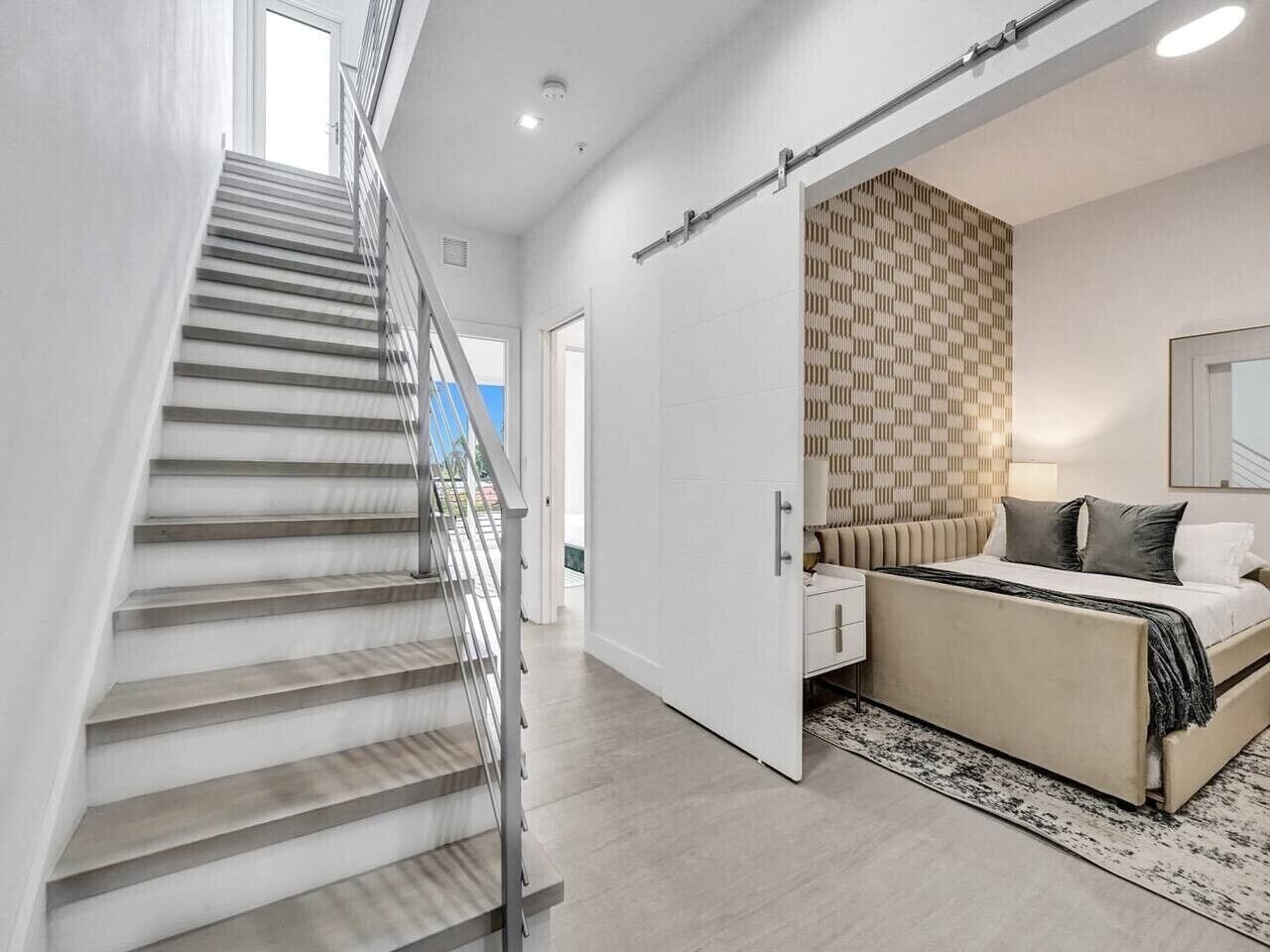 A modern bedroom with a staircase, a bed with a patterned headboard, and a view of the outdoors.