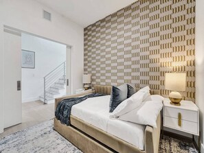 Ein modernes Schlafzimmer mit Bett, Nachttischen, einer Wand mit Muster und einer Treppe, die in einen anderen Raum führt.
