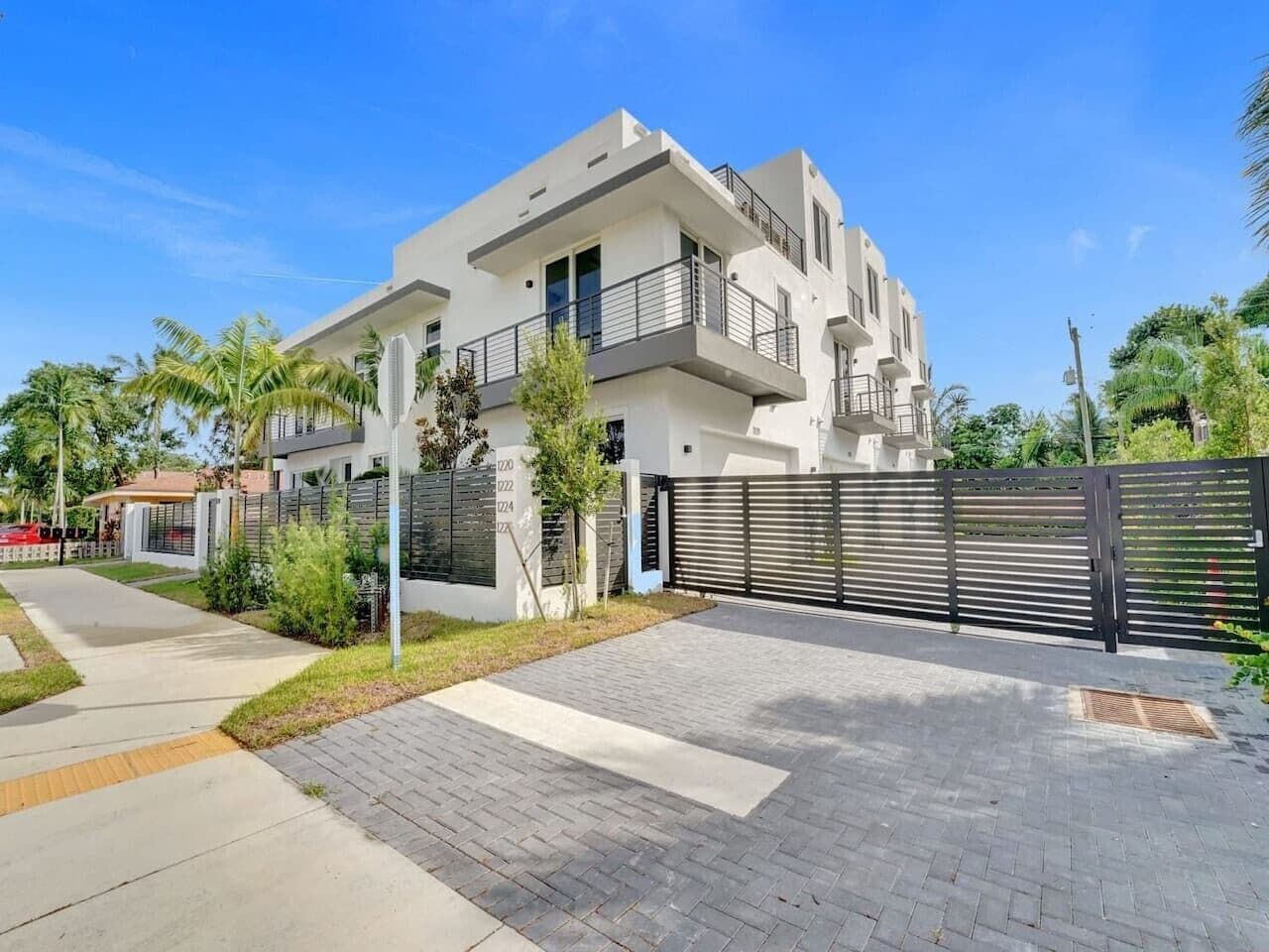 A modern two-story house with a paved driveway, a gated entrance, and a balcony.