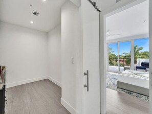 Ein modernes Hotelzimmer mit einer großen Schiebeglasdoor zu einem Balkon mit Blick auf Palmen und ein Gebäude.