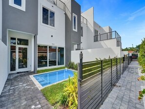A modern two-story building with a swimming pool, a gated entrance, and a paved walkway. - New Ft Lauderdale Luxe Home + Pool near Las Olas (Fort Lauderdale)
