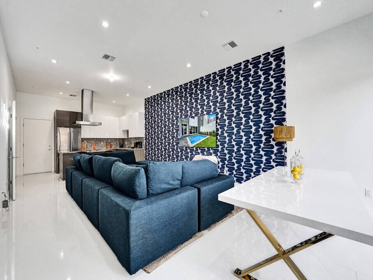 A modern living room with a blue sofa, a white dining table, and a patterned wall.