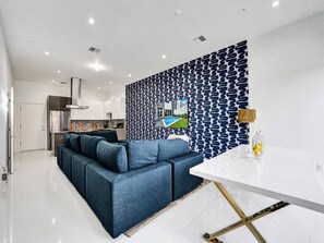 A modern living room with a blue sofa, a white dining table, and a patterned wall. - New Ft Lauderdale Luxe Home + Pool near Las Olas (Fort Lauderdale)