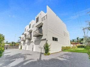 A modern multi-story residential building with balconies, a paved driveway, and a well-maintained lawn. - New Ft Lauderdale Luxe Home + Pool near Las Olas (Fort Lauderdale)