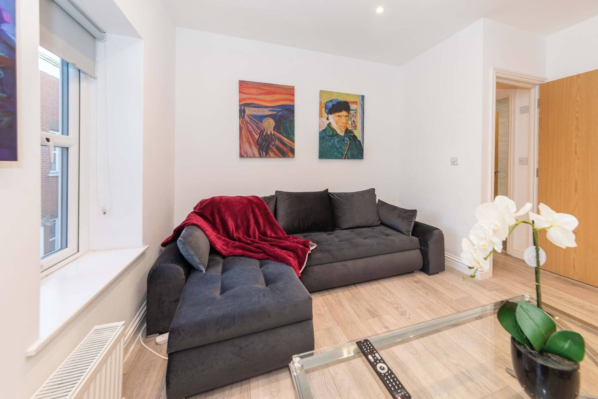 Ein modernes Wohnzimmer mit einem grauen Ecksofa, einer roten Decke und zwei Bildern an der Wand.