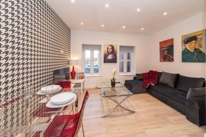 A modern living room with a glass coffee table, a black sofa, and a dining area with a red table runner. - Ibex House Modern 2-bed Flat Free Parking (Reading)