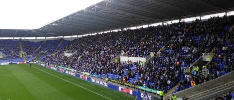 A stadium with tiered seating, a green field, and various advertisements.