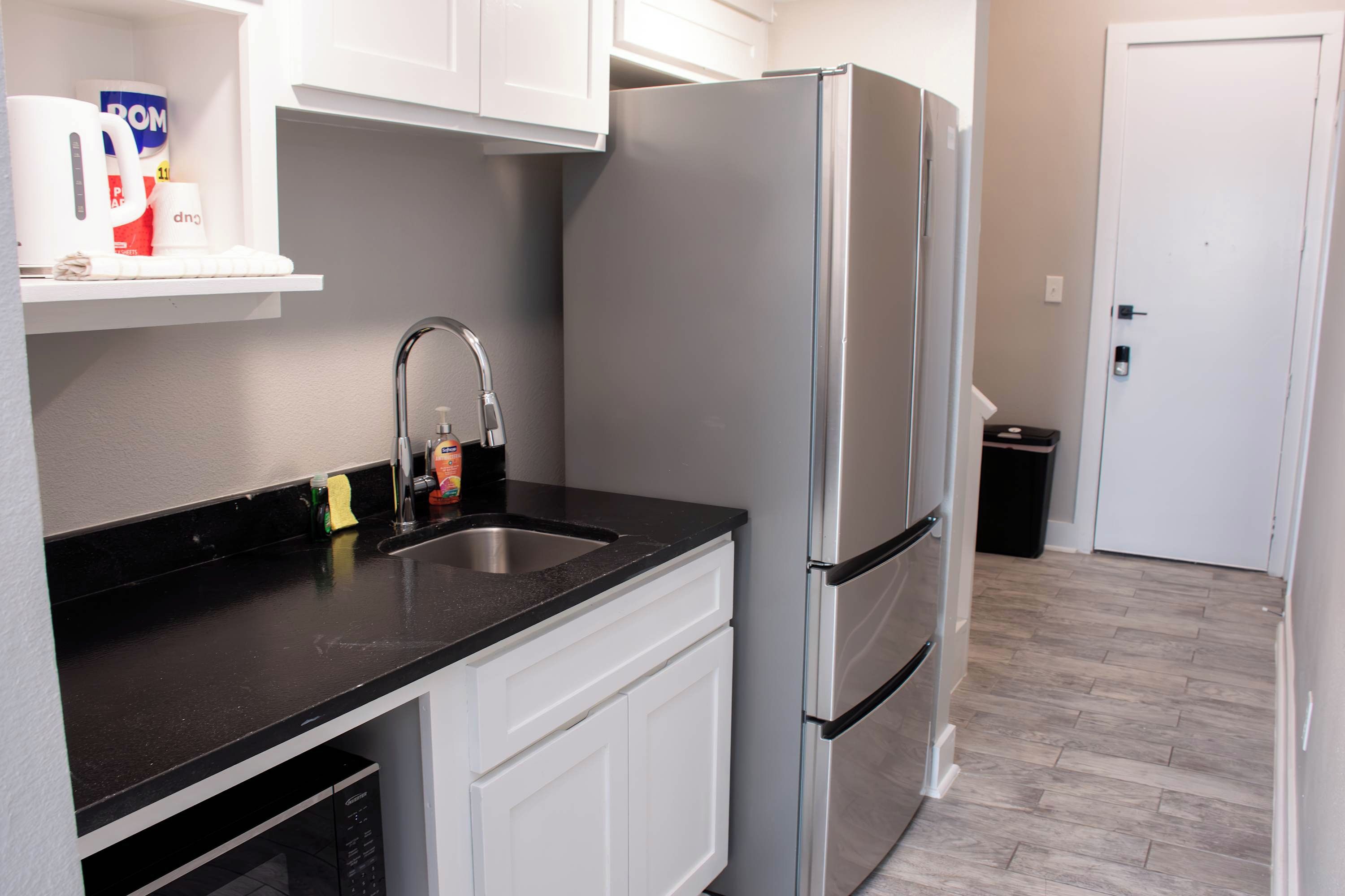 Una cocina moderna con un refrigerador de acero inoxidable, una encimera negra y armarios blancos.