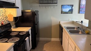 A kitchen with a stove, oven, refrigerator, and a sink. There are wine glasses on a shelf above the refrigerator.