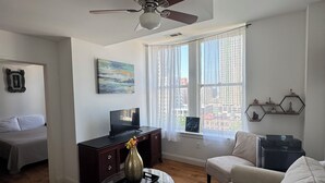 A living room with a ceiling fan, a sofa, a coffee table with a vase, a TV on a stand, and a window with curtains.