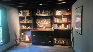 Ein Zimmer mit Holzboden, einem Schreibtisch, einer Gitarre, Regalen mit Büchern und Dekoration sowie einer Tafel an der Wand.