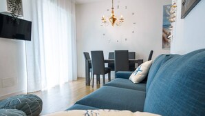 A modern living room with a sofa, a dining table with chairs, a chandelier, and a large window with curtains. - Unique property: 120 square meters - 150 meters from the beach - garage (Lido di Jesolo)