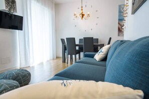 A modern living room with a sofa, a dining table with chairs, a chandelier, and a large window with curtains. - Unique property: 120 square meters - 150 meters from the beach - garage (Lido di Jesolo)