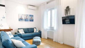 A modern living room with a blue sofa set, a small ottoman, and a flat-screen TV mounted on the wall. - Unique property: 120 square meters - 150 meters from the beach - garage (Lido di Jesolo)