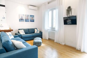 A modern living room with a blue sofa set, a small ottoman, and a flat-screen TV mounted on the wall. - Unique property: 120 square meters - 150 meters from the beach - garage (Lido di Jesolo)