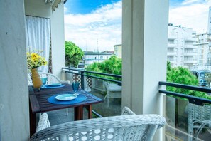A balcony with a table set for two, a vase of flowers, and a view of buildings and greenery. - Unique property: 120 square meters - 150 meters from the beach - garage (Lido di Jesolo)