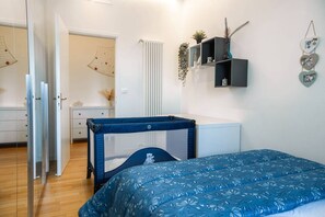 Een slaapkamer met een ledikant, een witte radiator, een plank met decoratieve objecten, en een deur die naar een andere kamer leidt.