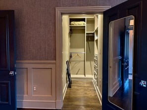 A walk-in closet with hanging space and shelves, a wooden floor, and a door leading to another room. - The Manor on Vermont, Historic DC Luxury Retreat (Washington)