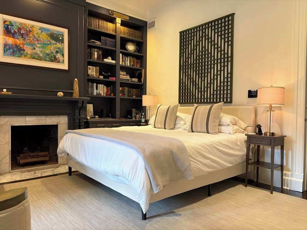 A bedroom with a large bed, a fireplace, a bookshelf, and a decorative wall panel.