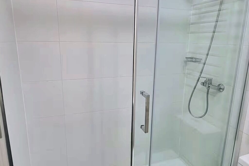 Een douchecabine met glazen wanden, een handdouche en een kraan op de muur.