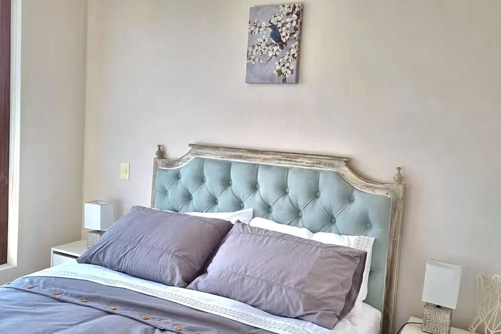 Ein Schlafzimmer mit einer gesteppten Kopfteil, einem Bett mit grauer Bettwäsche und einem an der Wand befestigten Kunstwerk.