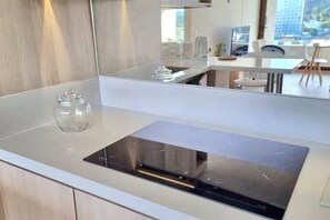 Une cuisine moderne avec une cuisinière intégrée, un bocal en verre posé sur le plan de travail et une vue sur la salle à manger à travers une grande fenêtre.