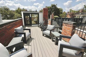 A rooftop deck with outdoor furniture, a glass door leading to an interior space, and a brick wall.