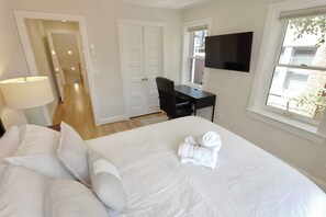 A hotel room with a bed, a desk, a chair, a TV, and a window.