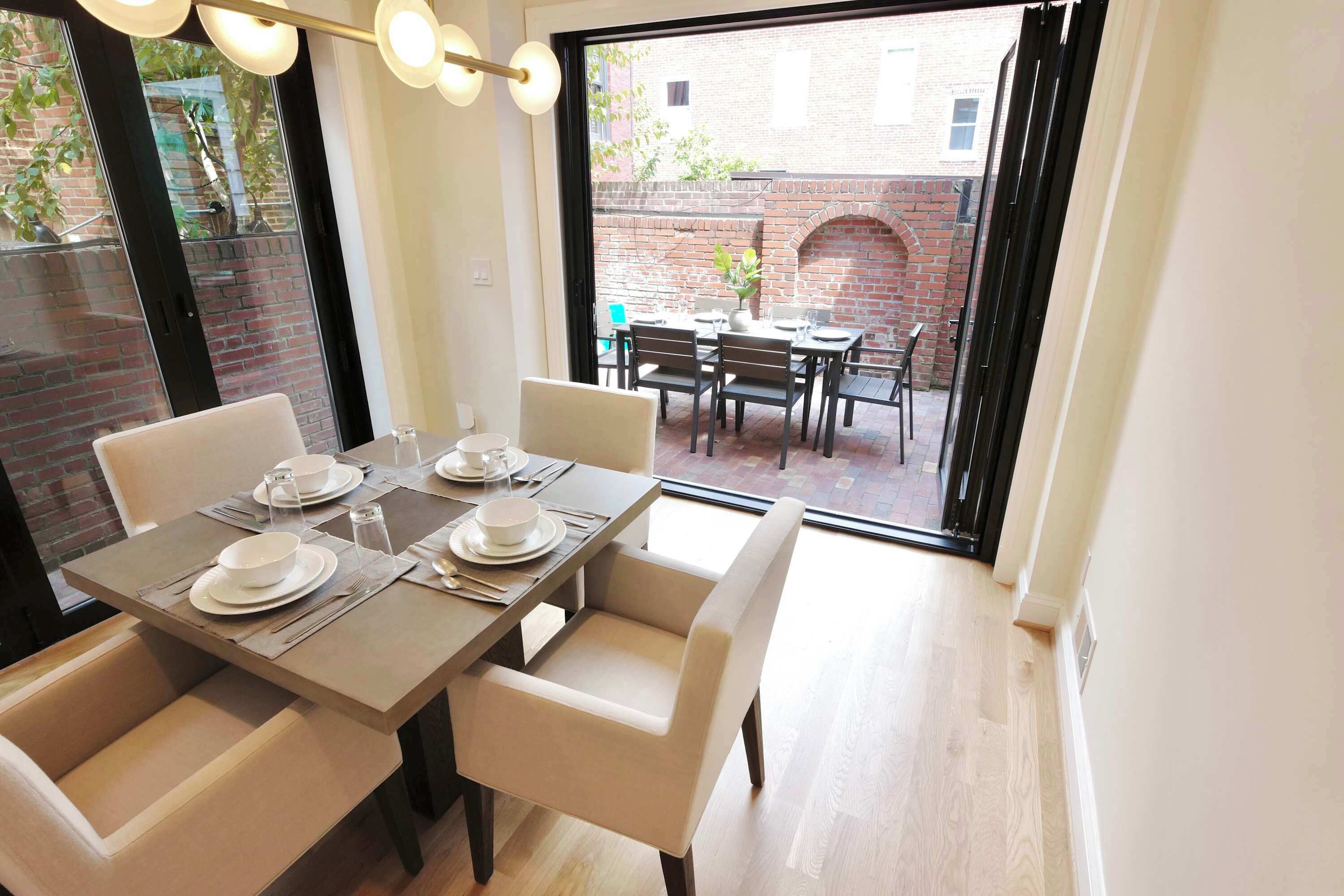 A dining area with a table set for four, chairs, and a view of the outside.