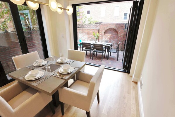 A dining area with a table set for four, chairs, and a view of the outside.