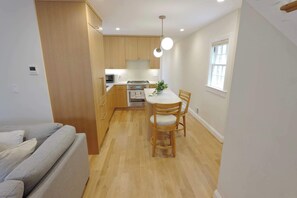 A modern kitchen with wooden cabinets, a dining table with chairs, a built-in oven, and a microwave. - Stunning Georgetown Townhouse, Rooftop Oasis (Washington)