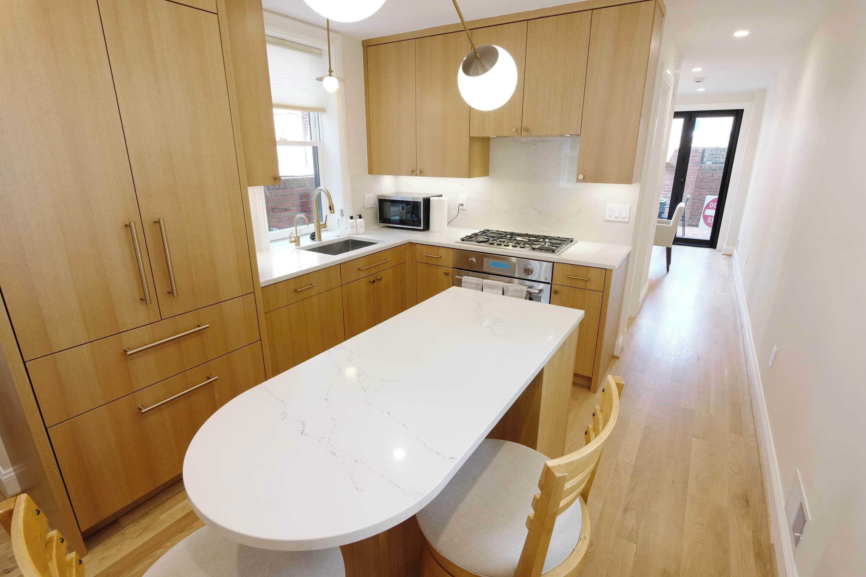 Une cuisine moderne avec des meubles en bois, un plan de travail en marbre blanc, un four à micro-ondes encastré et une cuisinière à gaz.