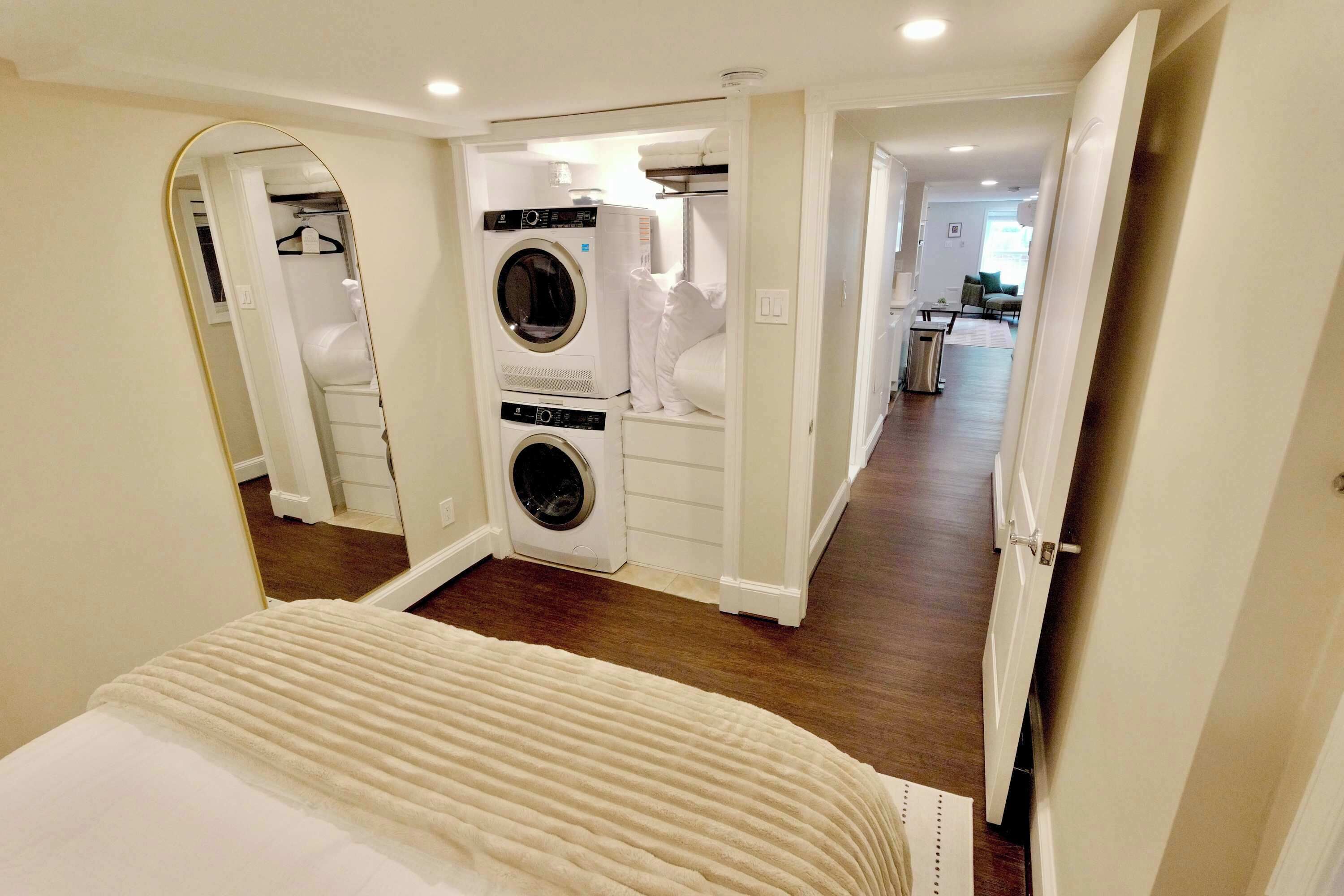 A bedroom with a bed, a walk-in closet with a washing machine, and a hallway leading to a bathroom.