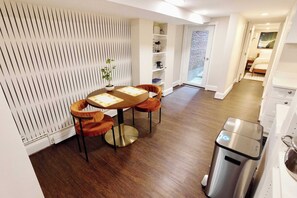 A modern kitchen with a dining area, featuring a round table with chairs, a built-in shelf unit, and a trash bin. - Charming Retreat on Swann (Washington)