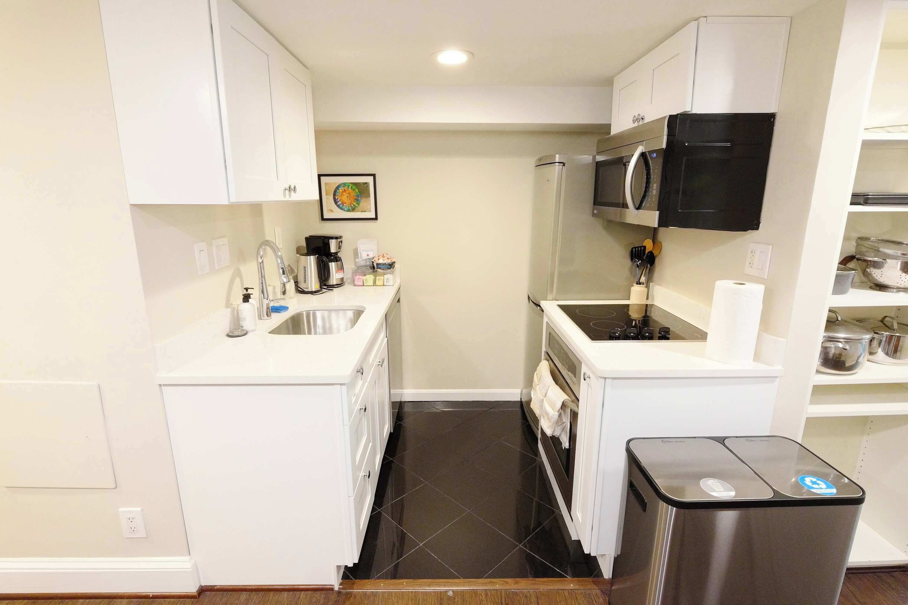 A compact kitchen with white cabinetry, a microwave, a stove, and a trash bin.
