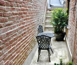 A narrow outdoor space with a brick wall, a metal table with chairs, and a potted plant. - Charming Retreat on Swann (Washington)
