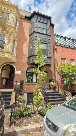 A multi-story building with a brick facade, a central staircase, and a tree in the front yard. - Charming Retreat on Swann (Washington)