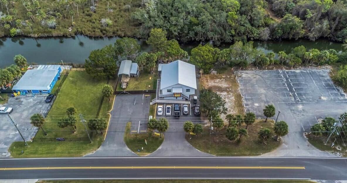 An aerial view of a property with a large building, parking lot, and a body of water.