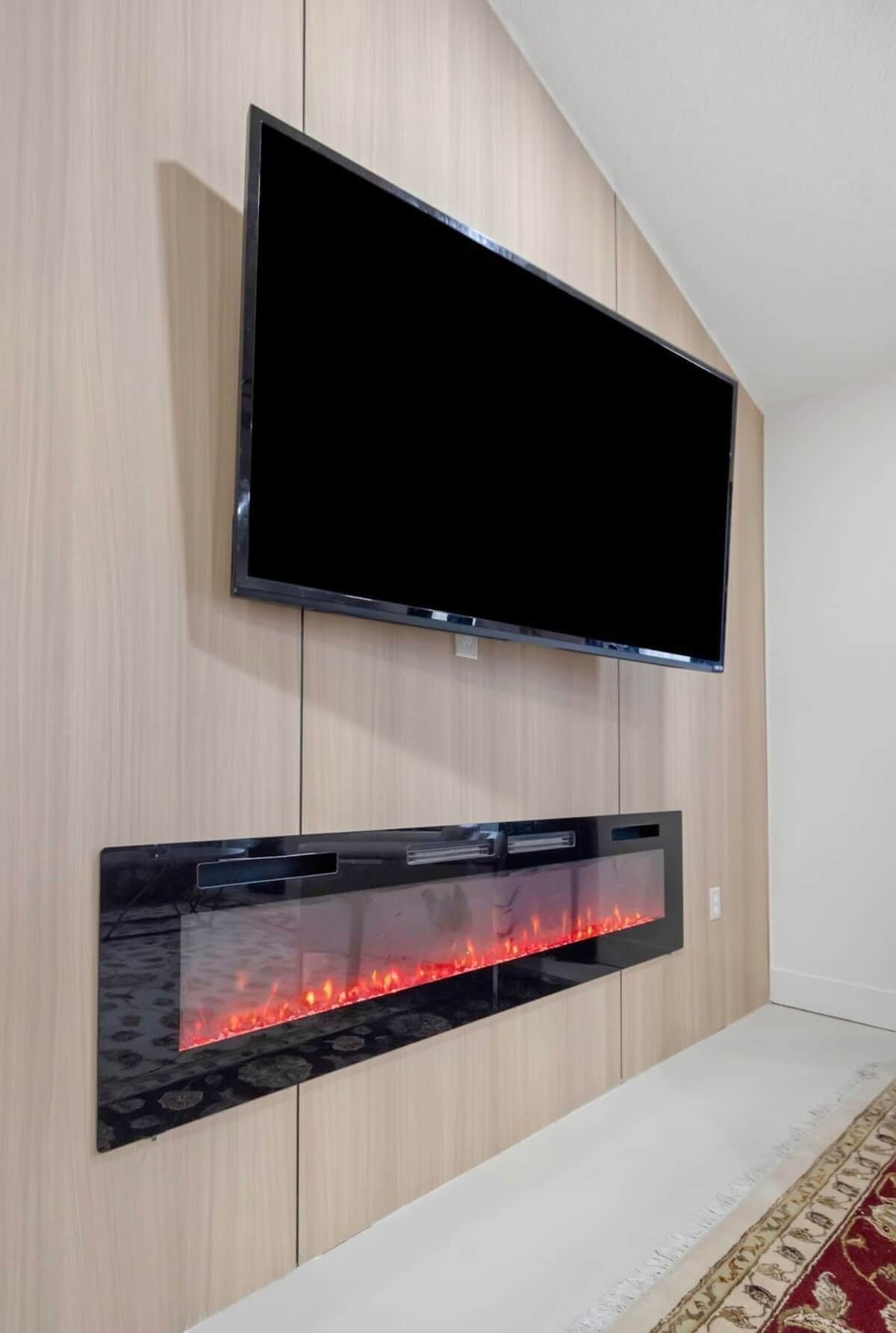 Ein Flachbildfernseher über einem Kamin mit Glasfront, hinter dem die Flammen sichtbar sind.
