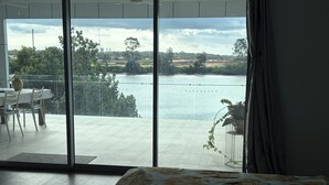 Ein Zimmer mit einer großen Schiebeglasdoor, die auf einen Balkon mit Blick auf ein Gewässer und viel Grün führt.