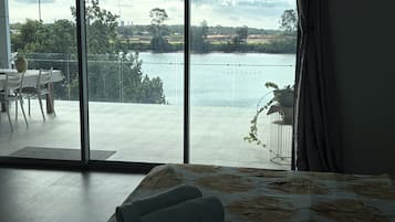A room with a large sliding glass door leading to a balcony overlooking a body of water and greenery.