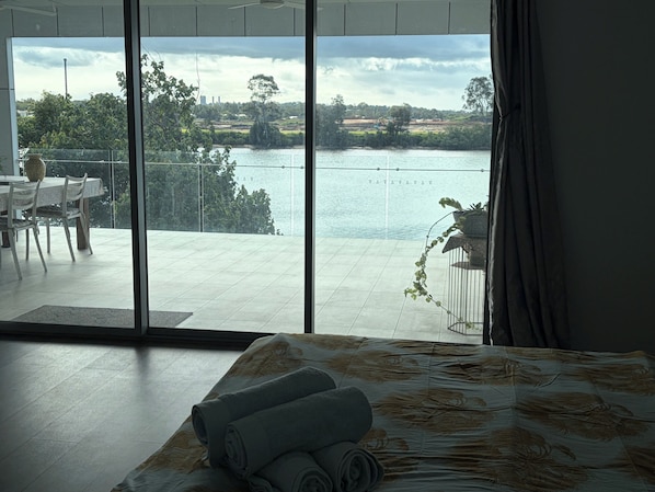 A room with a large sliding glass door leading to a balcony overlooking a body of water and greenery.
