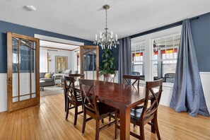 A dining area with a wooden table and chairs, a chandelier, and a view of the living room through an open door. - Walk to Mayo Clinic! Luxury Furnished 4-bedroom house. Perfect for families (Rochester)